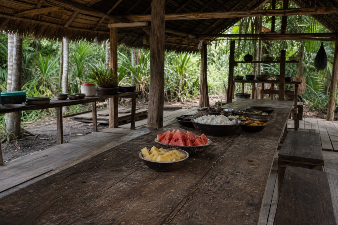 Simple wooden dining hall with fresh fruit and rice on a long table at a budget jungle retreat