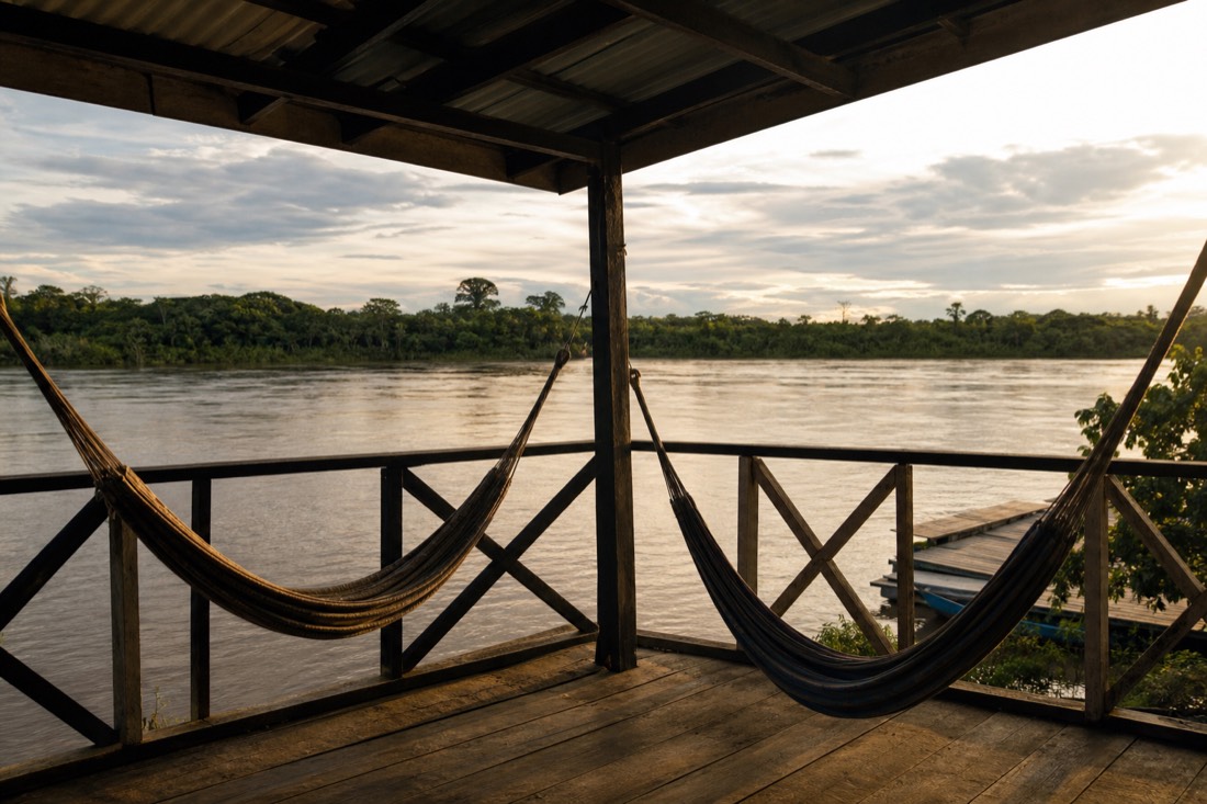 Two hammocks on a wooden veranda above a calm Amazon tributary in late afternoon light