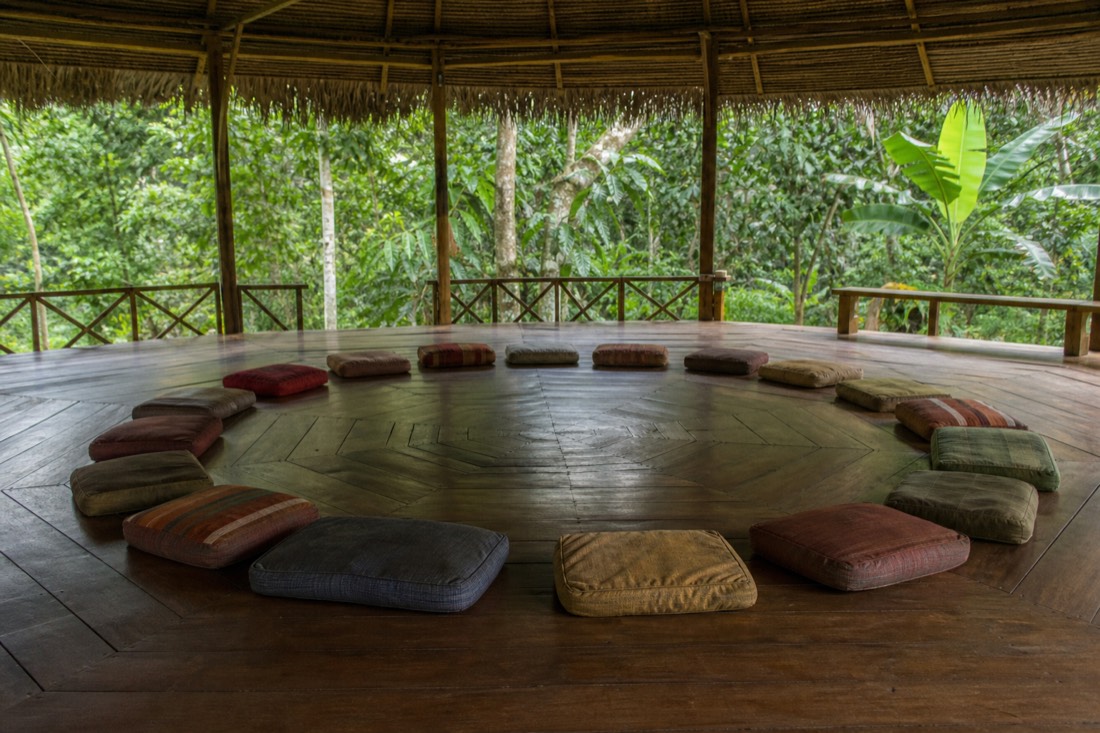 Empty sharing circle of floor cushions in an open-air jungle pavilion during daytime