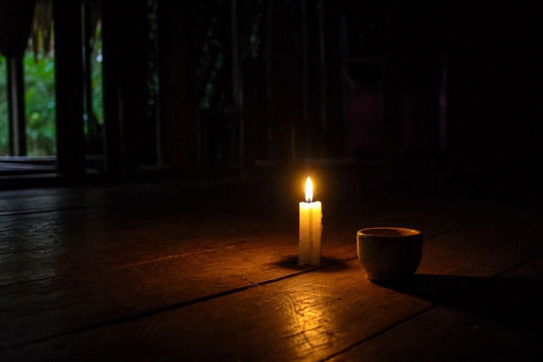 Single lit candle on the wooden floor of a dark ceremony space with a cup beside it