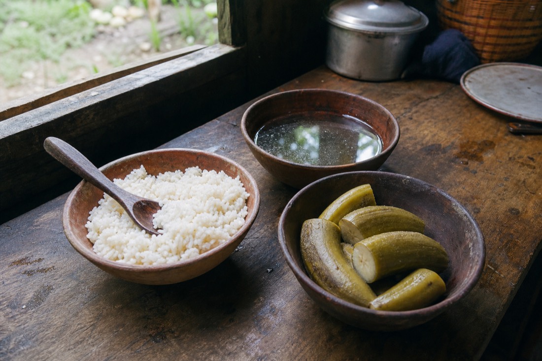 Simple meal of rice, green plantain and broth in clay bowls on a wooden kitchen counter, morning light, Tamshiyacu region
