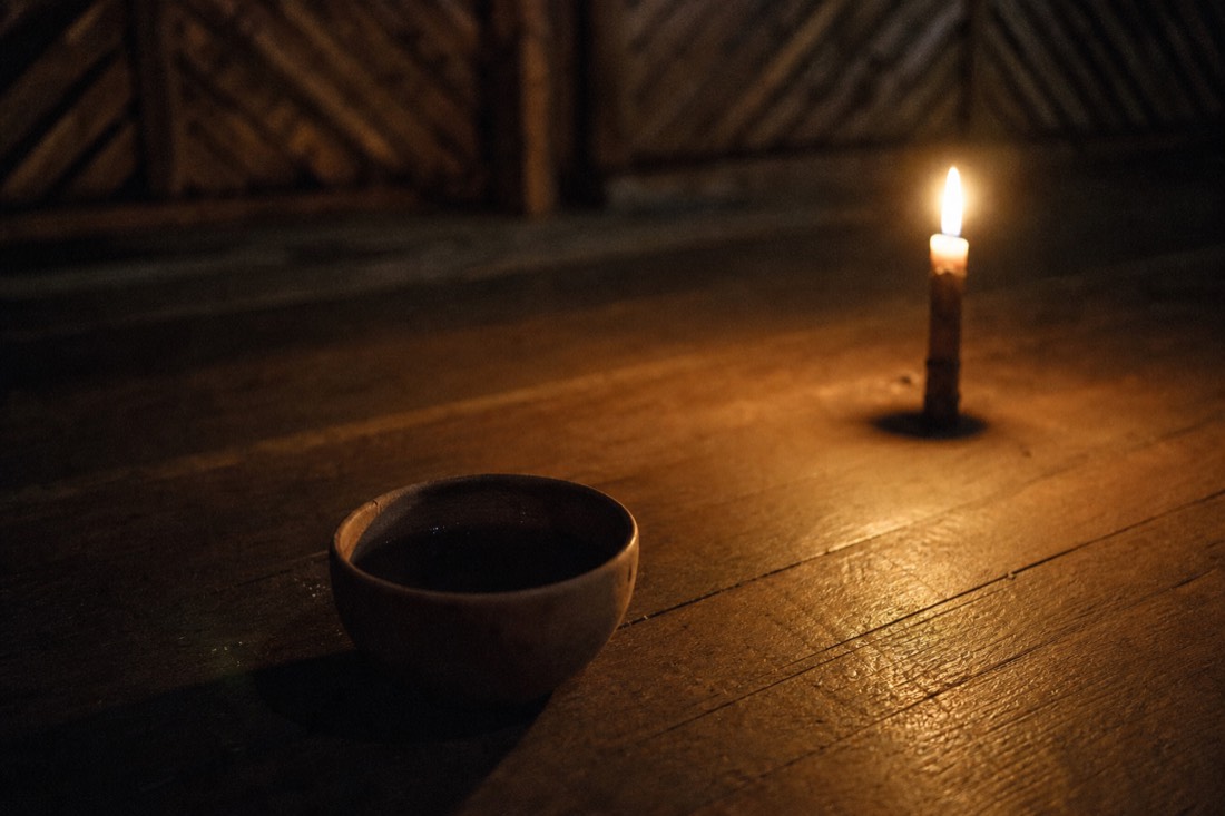 Candlelit cup of dark ayahuasca brew on the wooden floor of a maloca at night