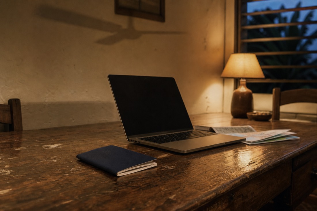 Passport, laptop and folded papers on a guesthouse desk in warm lamplight