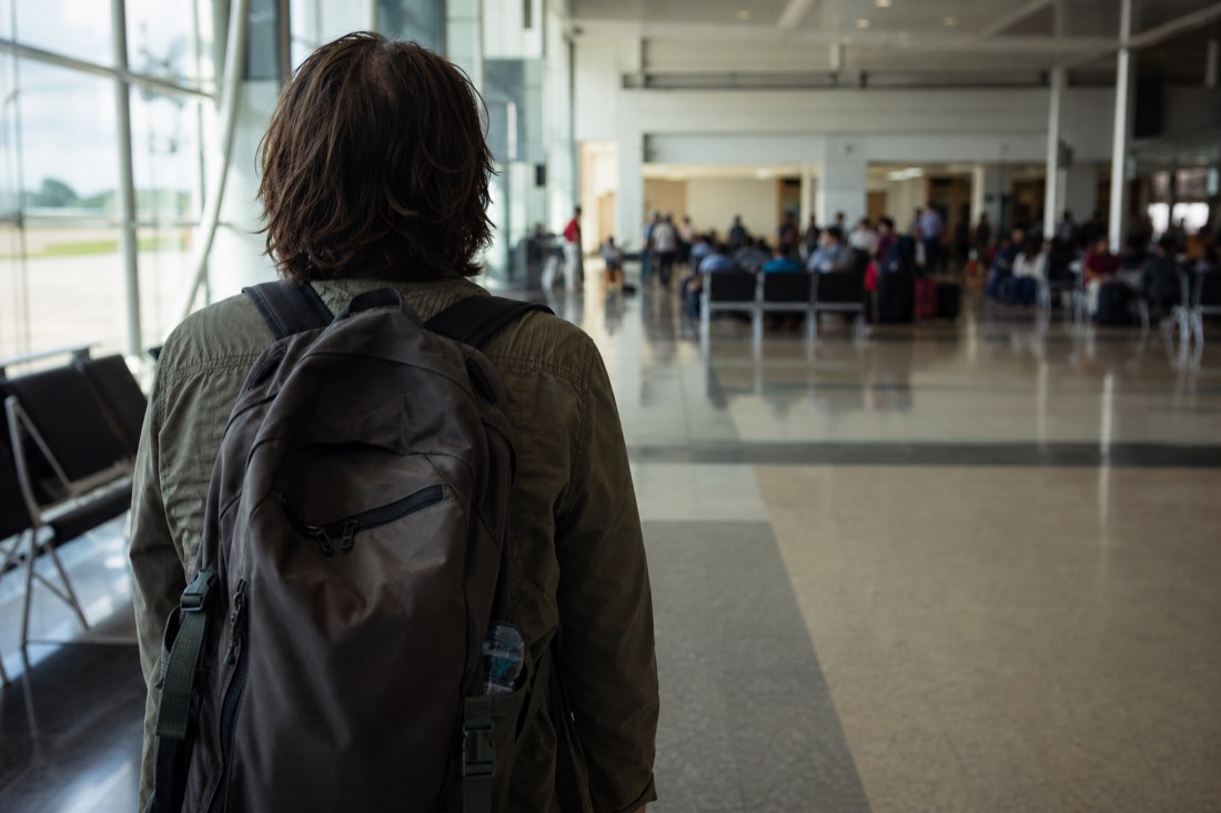 Airport departure hall with a single traveler and a backpack, seen from behind in soft light