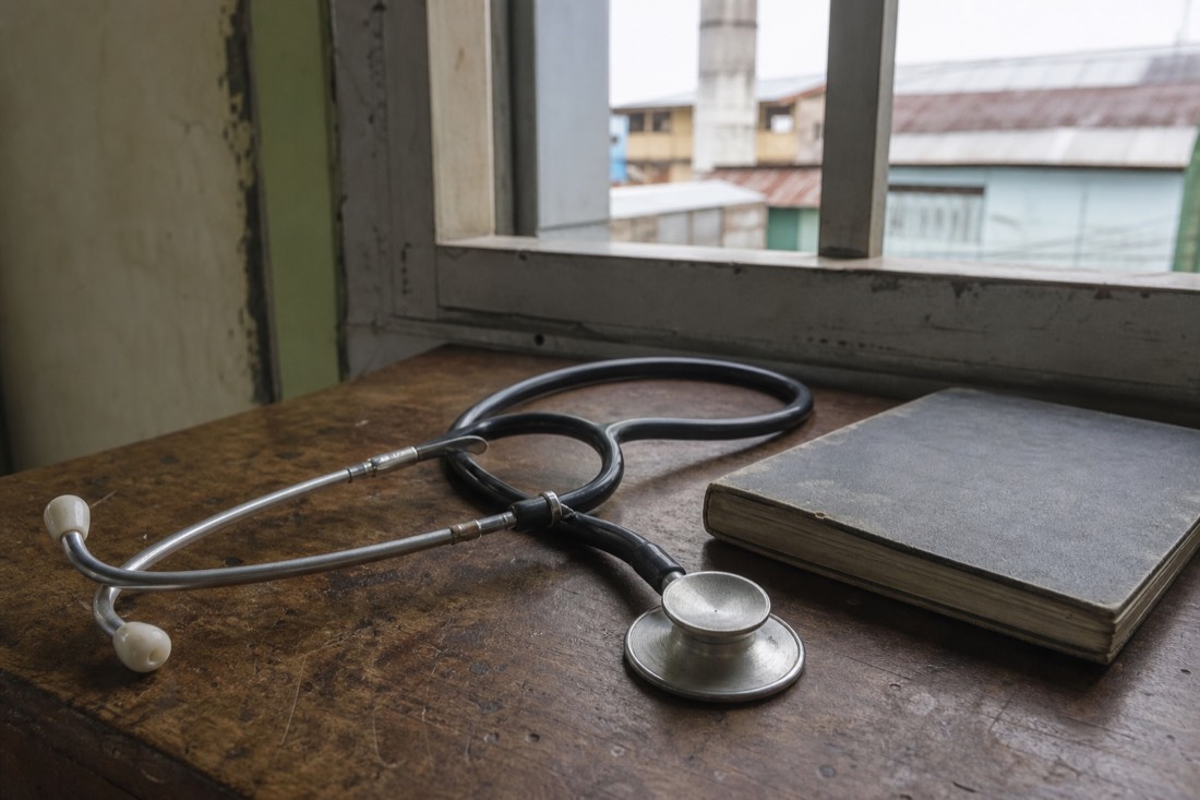 Stethoscope resting on a worn wooden table beside a closed notebook in soft side light
