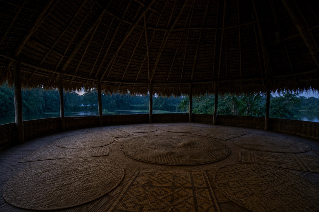 Empty ceremonial maloca interior with woven mats arranged in a circle at dusk
